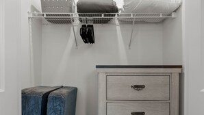 A closet with a white dresser, a blue bench, and a shelf with folded blankets and a black hanger.