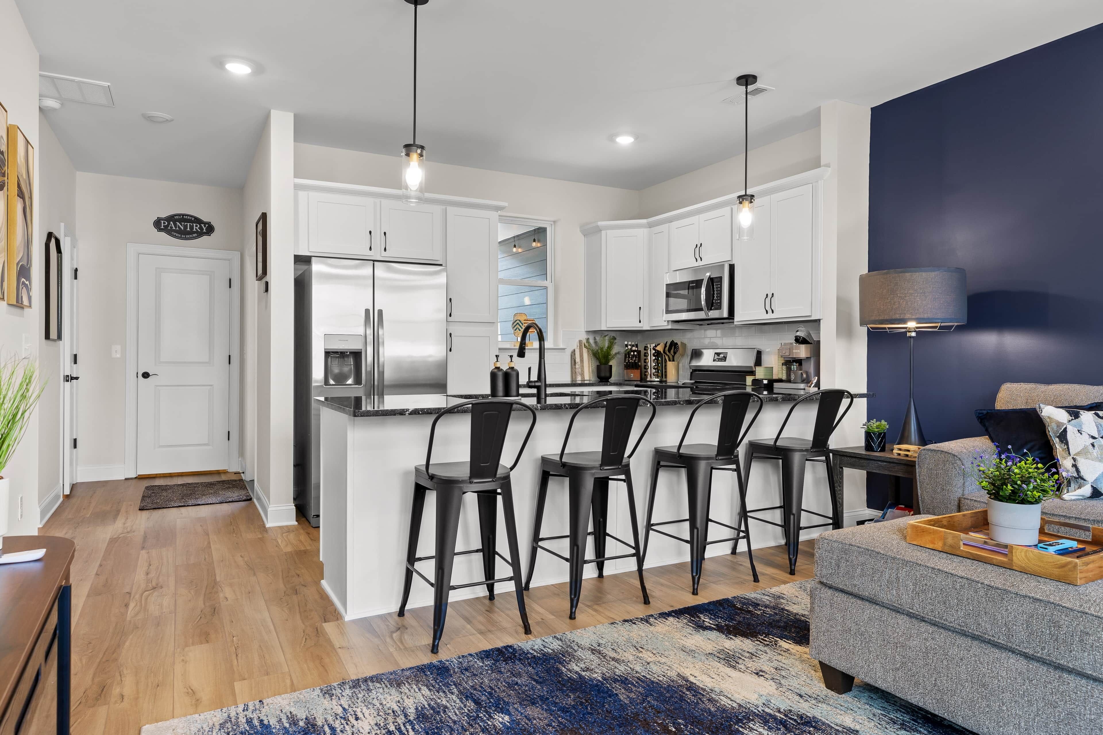 A modern kitchen with white cabinets, stainless steel appliances, and black bar stools.
