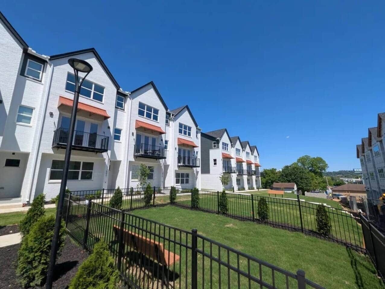 A row of modern residential buildings with balconies, a well-maintained lawn, and a clear sky.