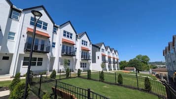 A row of modern residential buildings with balconies, a well-maintained lawn, and a clear sky.