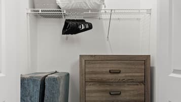 A hallway with a wooden chest of drawers, a metal shelf with folded items, and a large blue object.