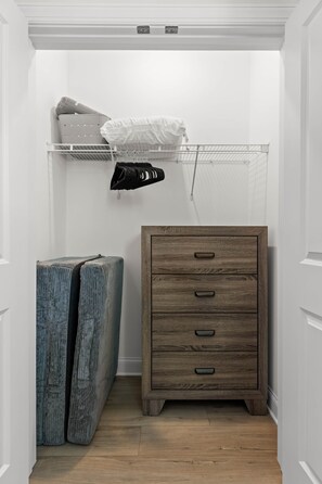 Un pasillo con un aparador de madera, un estante metálico con objetos doblados y un objeto azul grande.