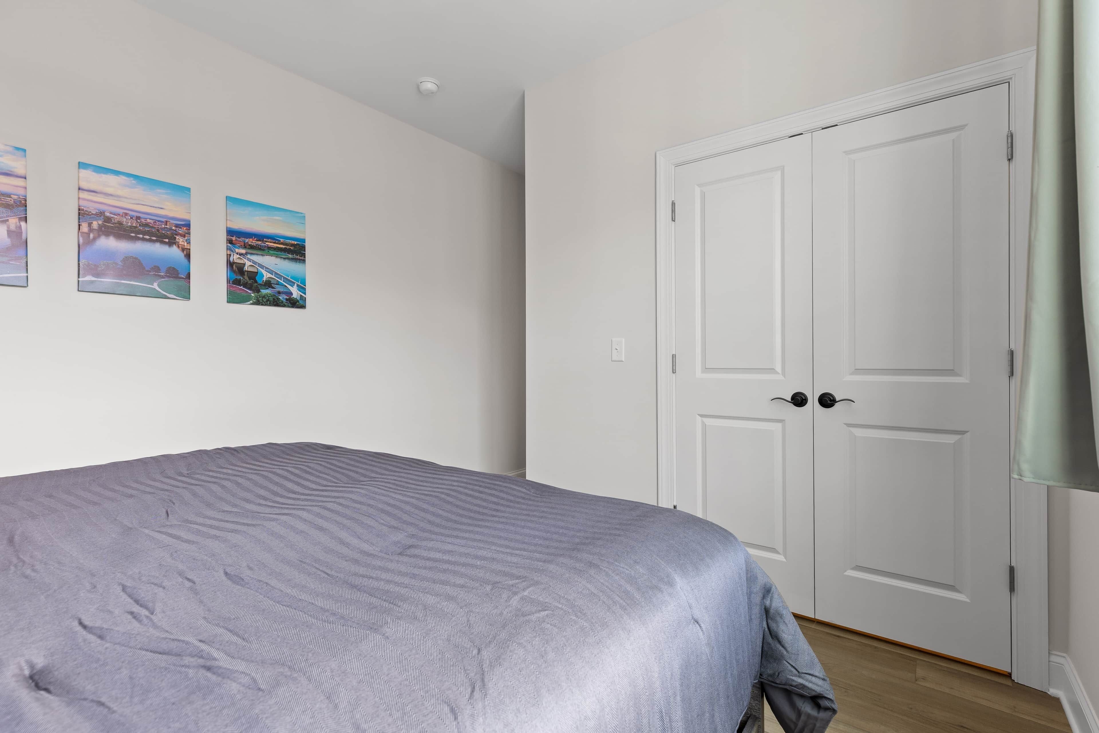 A bedroom with a bed, two doors, and two landscape paintings on the wall.