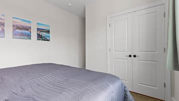 A bedroom with a bed, two doors, and two landscape paintings on the wall.