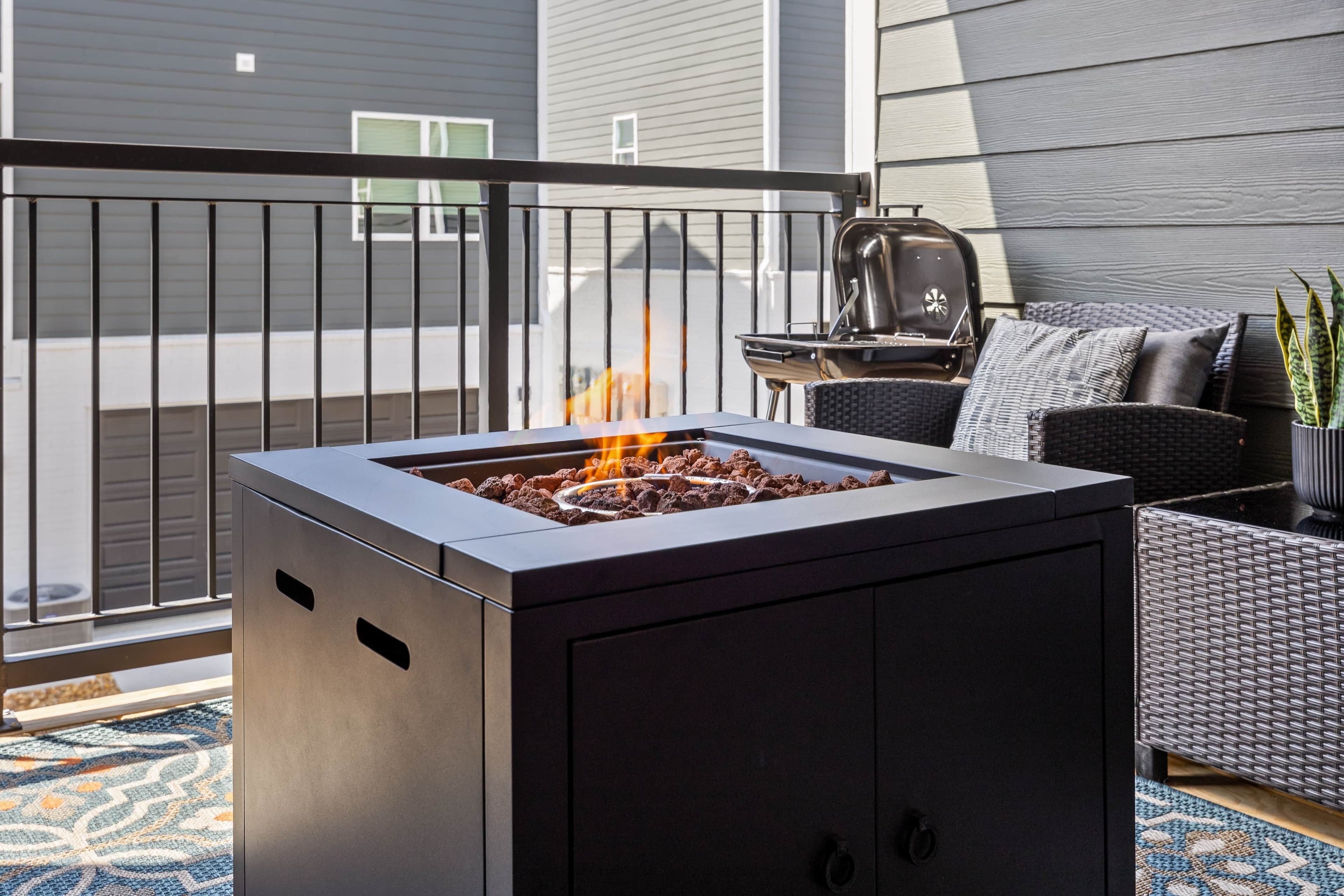 A modern outdoor fire pit with a metal grill, surrounded by a balcony railing.