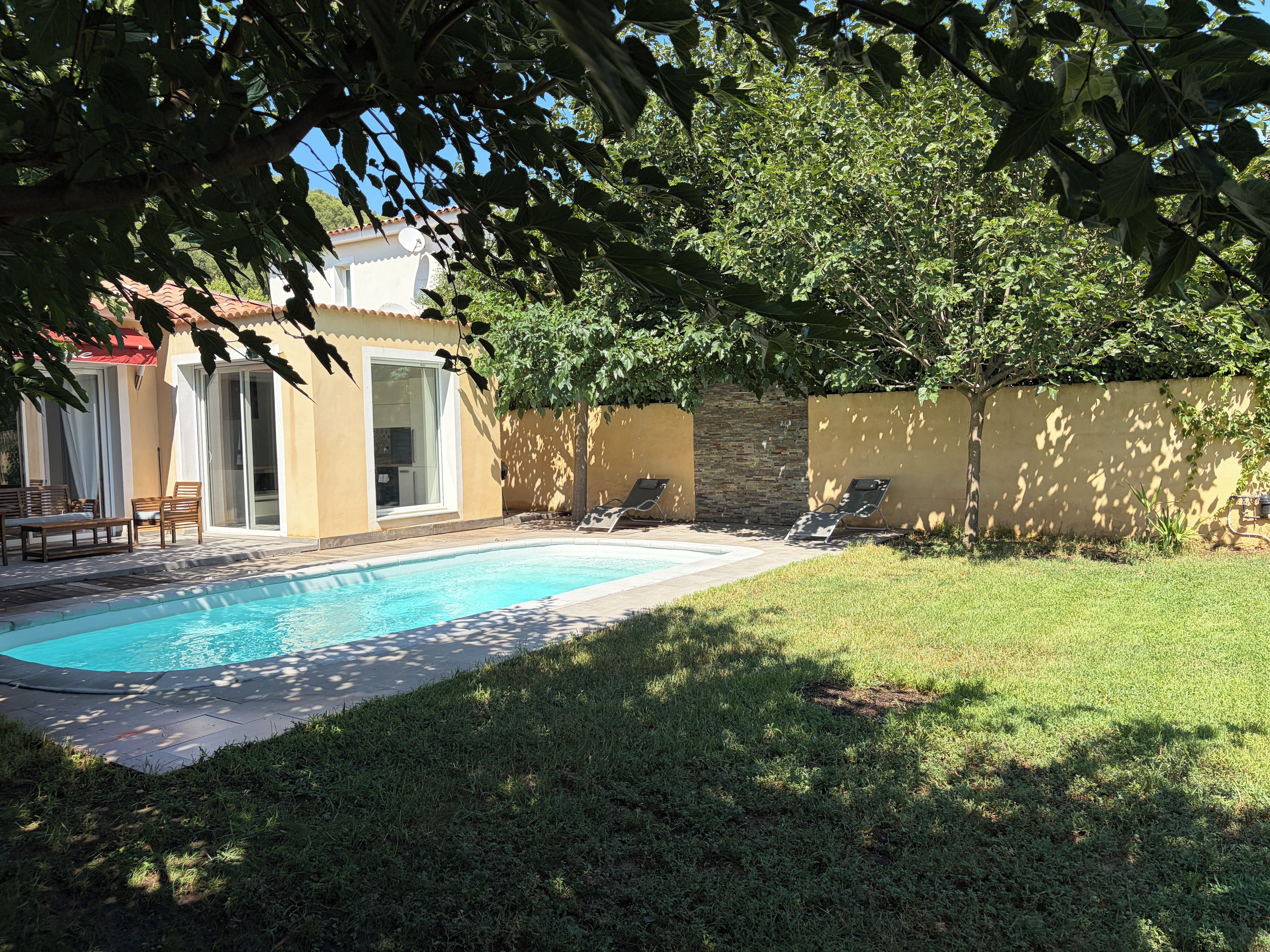 A swimming pool with lounge chairs, a patio area, and a building with a tiled roof.