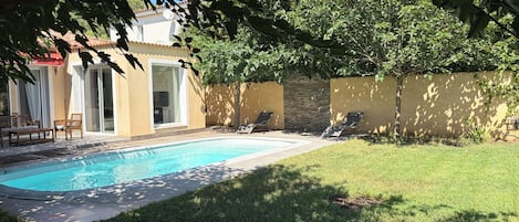 Una piscina con sillas de descanso, un área de patio y un edificio con tejado de azulejos.