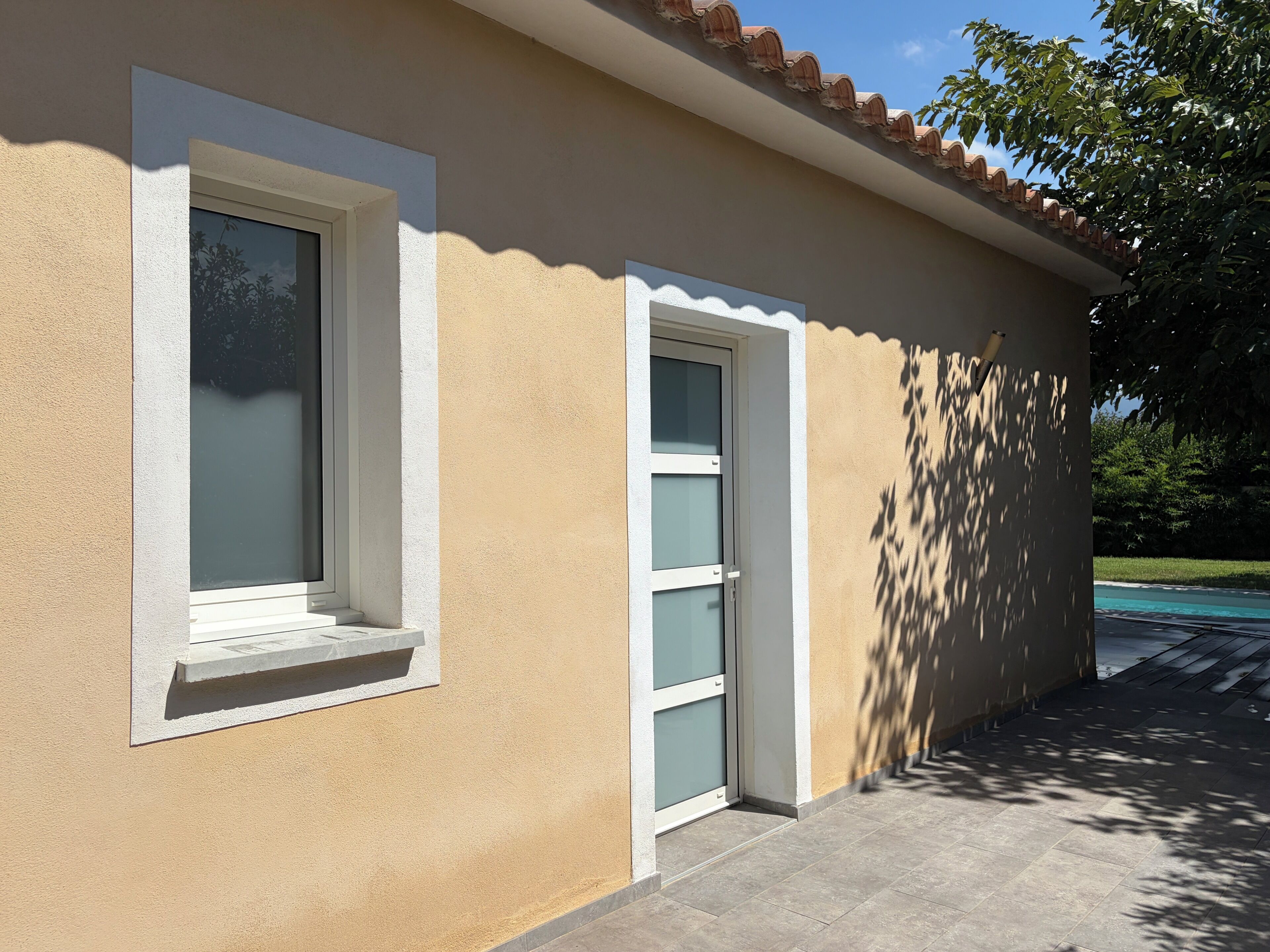 A building with a beige exterior, a window with a white frame, and a door with a white frame.