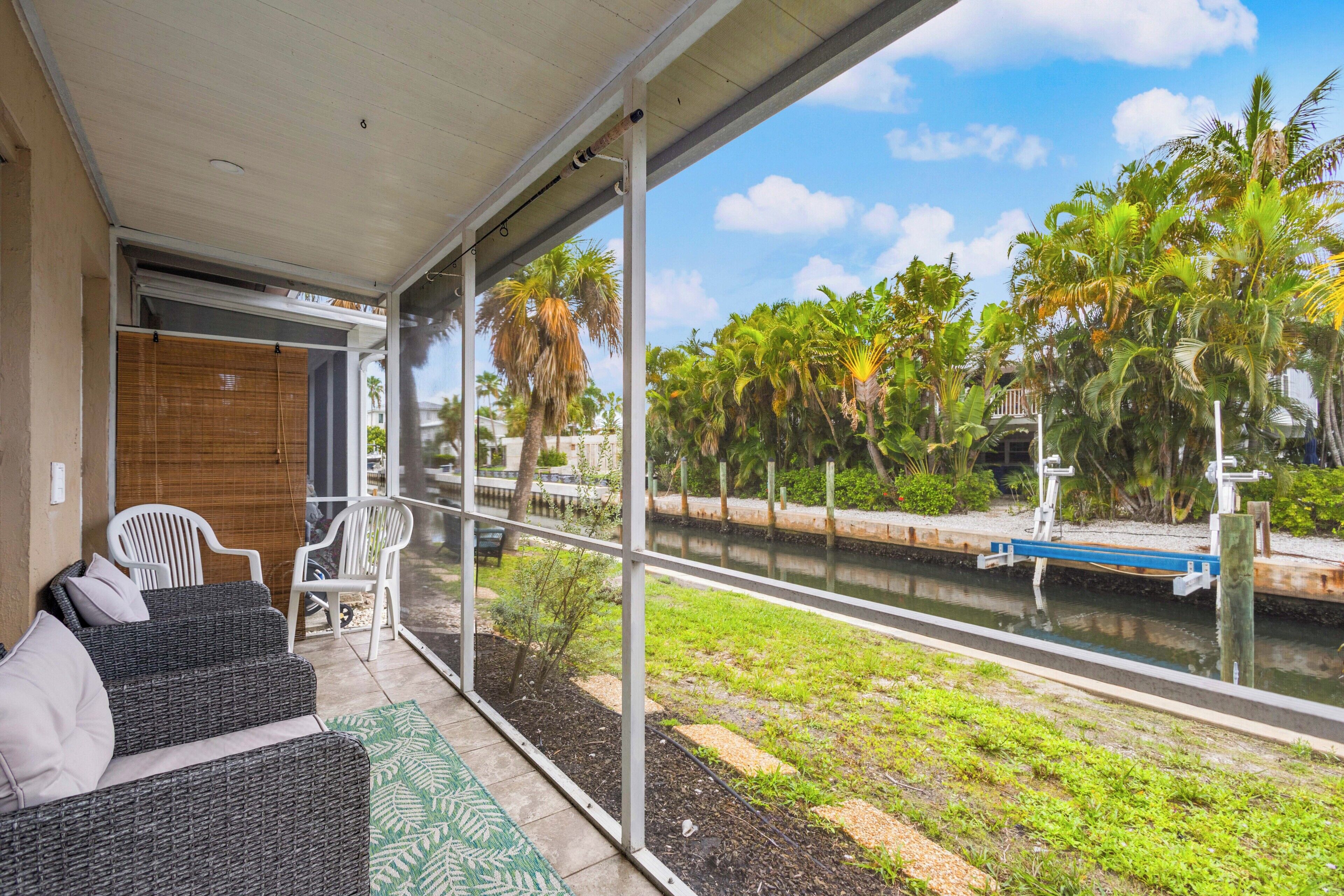 A balcony with wicker furniture, a view of a canal with palm trees, and a clear sky.
