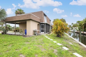 Ein Wohnhaus mit überdachter Terrasse, kleinem Garten und einem Kanal.