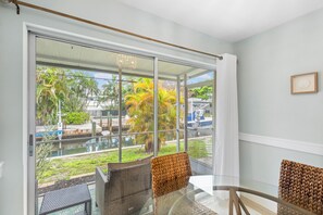 Ein Zimmer mit Glastür, die zu einem Poolbereich führt, mit Korbmöbeln und einem gerahmten Bild an der Wand.