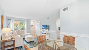 A modern living room with a glass coffee table, wicker chairs, a sofa, and a television on the wall. - The Salt House 2 BR / 1.5 BA Canal Front Home by RVA (Longboat Key)