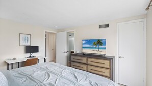 A bedroom with a bed, a desk, a dresser, and a television displaying a beach scene. - The Salt House 2 BR / 1.5 BA Canal Front Home by RVA (Longboat Key)