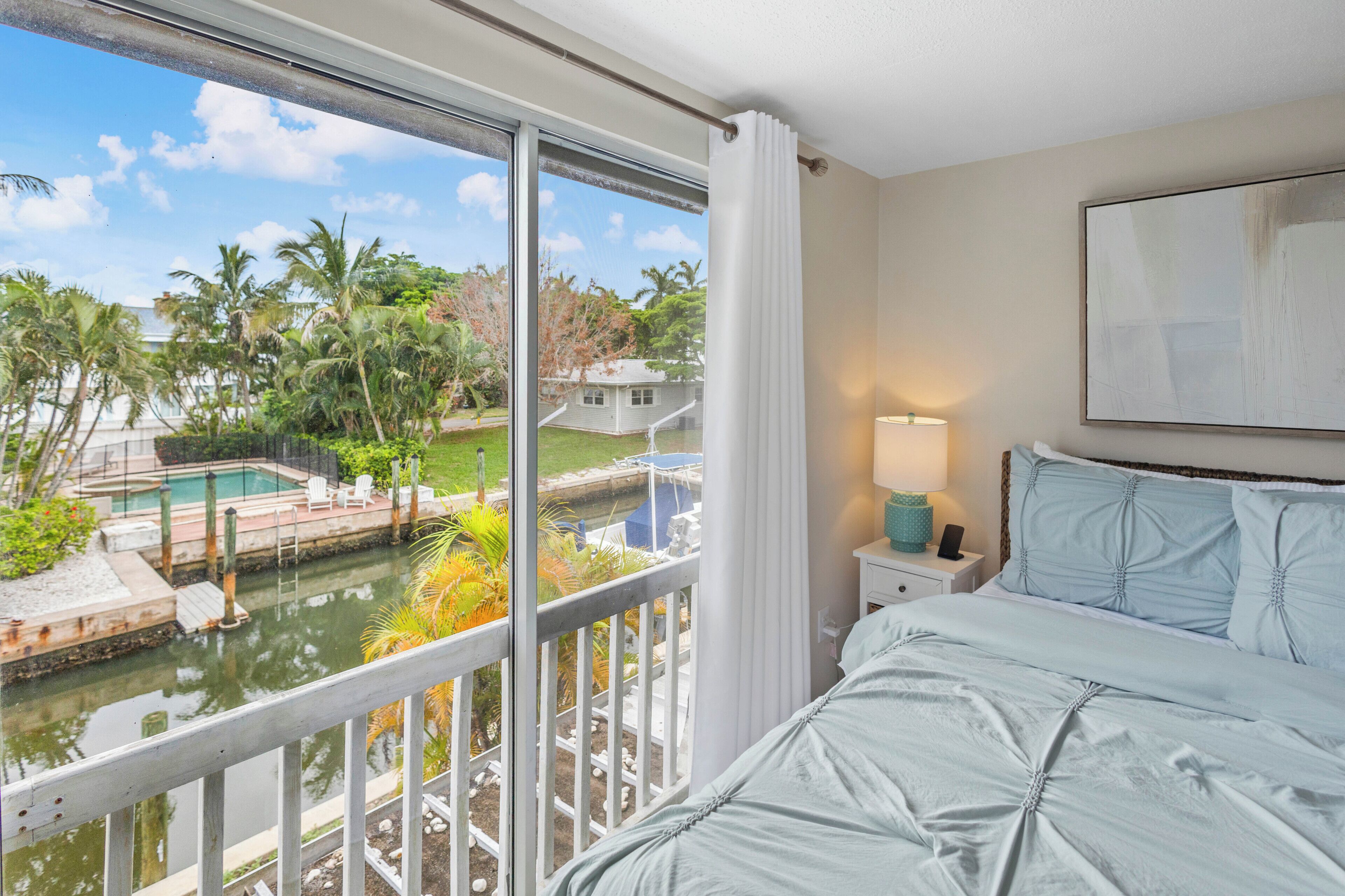 A hotel room with a large window overlooking a swimming pool and palm trees.