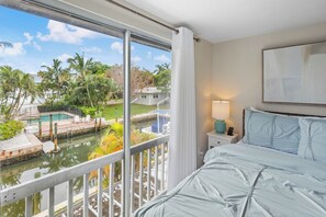 Hotelkamer met groot raam met uitzicht op een zwembad en palmbomen.