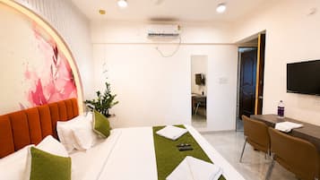 A hotel room with a bed, a desk, a chair, a television, and a bathroom visible through an open door.