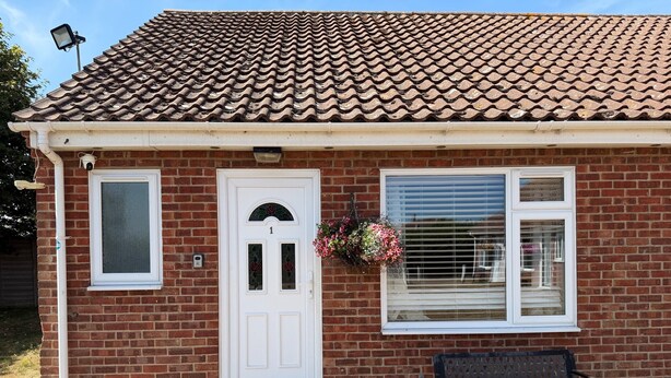 A brick house with a white door, a window with a flower basket, and a bench outside. - These quality bungalows are situated 200mt from Hemsby beaches and all ammenties (Gt Yarmouth)
