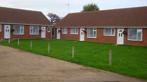 A row of brick houses with white doors and windows, a gravel driveway, and a grassy lawn. - These quality bungalows are situated 200mt from Hemsby beaches and all ammenties (Gt Yarmouth)