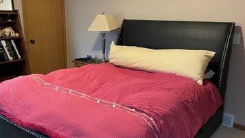 A bedroom with a bed, a nightstand, a lamp, a bookshelf, and a door.