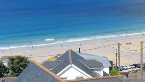 Vista costeira com praia, oceano e edifícios com telhados inclinados.