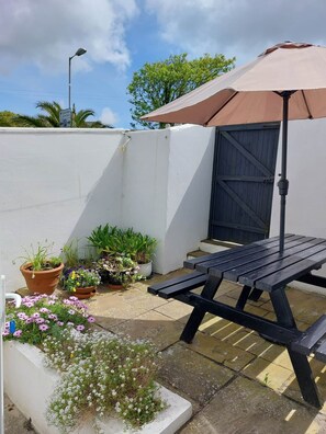 Eine Terrasse mit Tisch und Stühlen, umgeben von Topfpflanzen und einem überdachten Bereich.