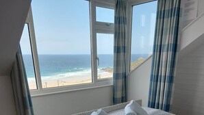 Quarto com uma cama, vista para a praia e janela com cortinas.