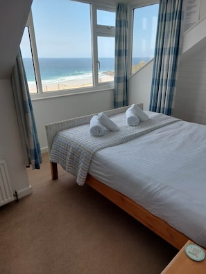 A bedroom with a bed, a view of the beach, and a window with curtains.