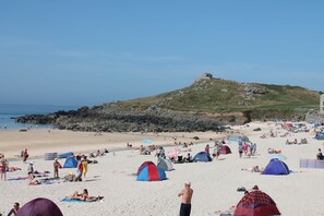 Ein Strand mit Zelten und Menschen, ein Hügel mit einer Bebauung und das Meer.