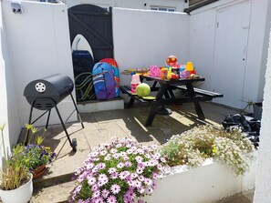 A patio with a barbecue grill, a table with children's toys, and potted flowers. - 14 Channel View, St. Ives, Cornwall TR26 1RG (St Ives)