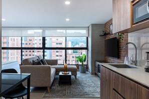 A modern kitchen with a large window, a sofa, and a dining area. - ENZO Privé | Studios - Modern Executive Suite in Laureles (Medellín)