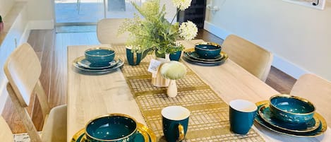 Un coin repas avec une longue table dressée pour six personnes, agrémenté de vaisselle turquoise et dorée, d’un set de table en fibres tressées et d’un vase rempli de fleurs.