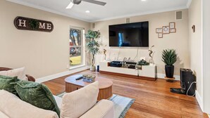 A living room with a flat-screen TV, a ceiling fan, and a 'HOME' sign on the wall.