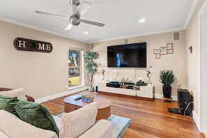 A living room with a flat-screen TV, a ceiling fan, and a 'HOME' sign on the wall.