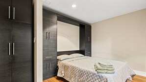 A bedroom with a bed, dark wooden wardrobe, and a white headboard.