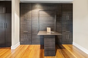 A room with dark wooden cabinets, a central table with a laptop, and a wooden floor. - The Breeze Stylish Home - Heat Pool (Carrollton)
