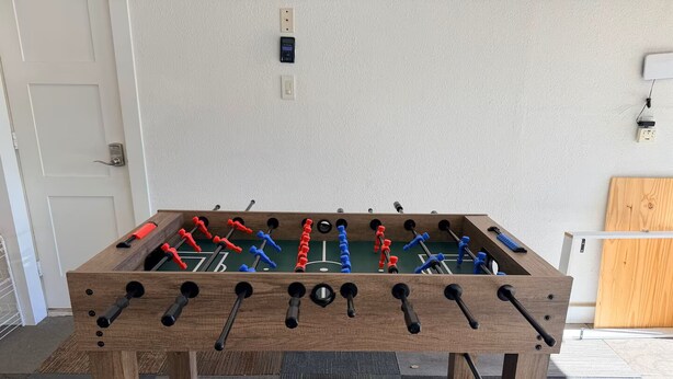 A wooden foosball table in a room with a door, electrical outlets, and a wooden panel on the wall.