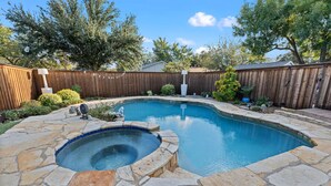 A backyard with a swimming pool, stone patio, wooden fence, and trees.