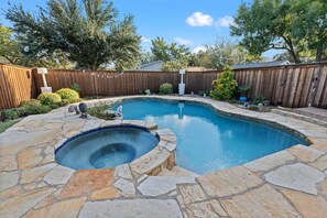 A backyard with a swimming pool, stone patio, wooden fence, and trees.