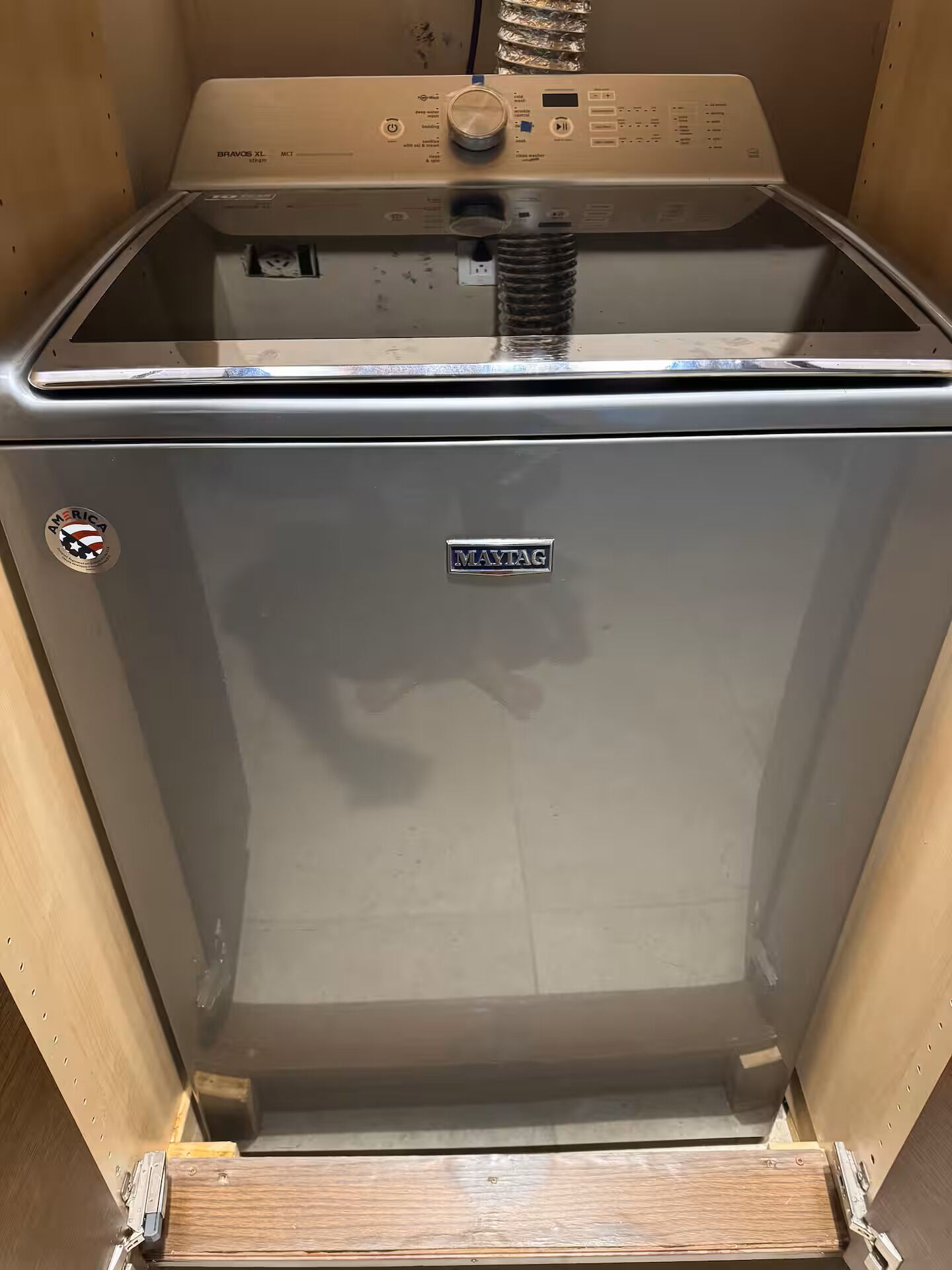 A compact, stainless steel appliance with a control panel, a Maytag logo, and a small American flag sticker.