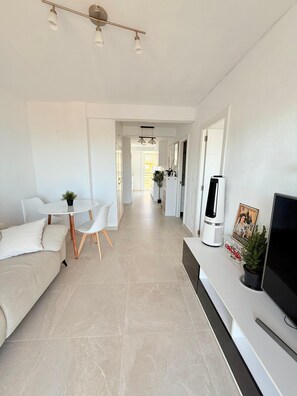 A modern living space with a sofa, a dining table with chairs, a flat-screen TV, and a potted plant. - Sea View Apartment with Terrace, Pool, and Padel Court | Miramar | 45 min from Valencia (Miramar)