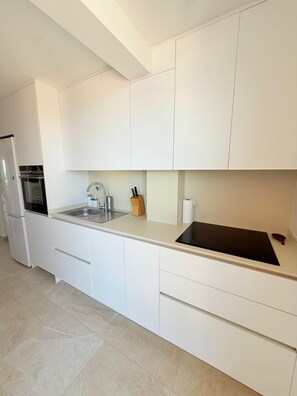 A modern kitchen with white cabinetry, a stainless steel sink, and a built-in oven. - Sea View Apartment with Terrace, Pool, and Padel Court | Miramar | 45 min from Valencia (Miramar)