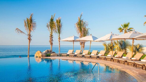 An infinity pool with lounge chairs and umbrellas, palm trees, and a view of the ocean. - Villa La Valencia (San José del Cabo)