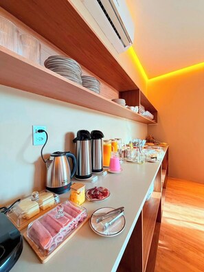 A breakfast buffet setup with various food items and beverages, a kettle, and a coffee maker.