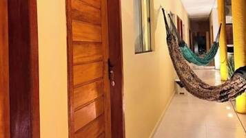 Un pasillo con una puerta de madera, una hamaca y un pilar amarillo.