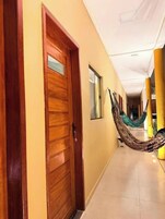 Un pasillo con una puerta de madera, una hamaca y un pilar amarillo.