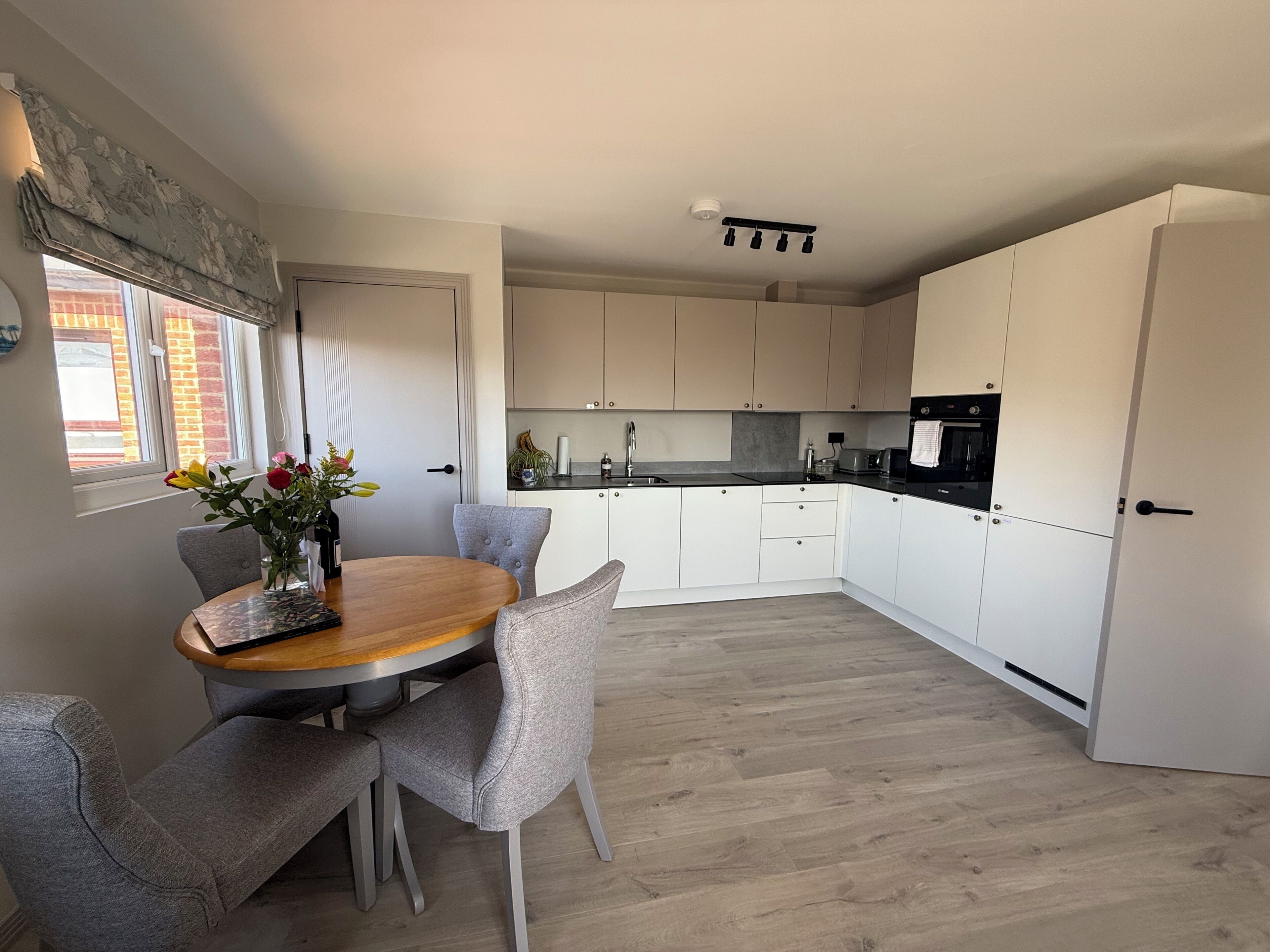 A modern kitchen with white cabinetry, a dining table with chairs, and a window with flowers.