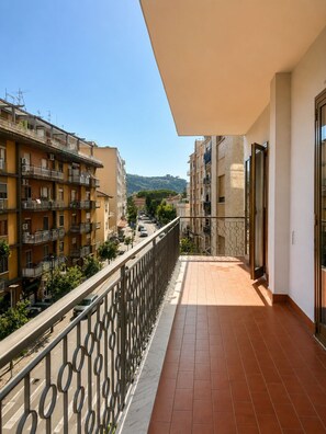 A balcony with a tiled floor and metal railing, overlooking a street with buildings and a hilly landscape. - Eolo's House—Sorrento (Sorrento)