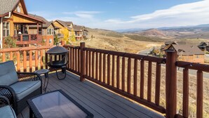 A wooden deck with outdoor furniture, a grill, and a view of a hilly landscape. - Beautiful 4-bedroom house in Granby perfect for your getaway (Granby)