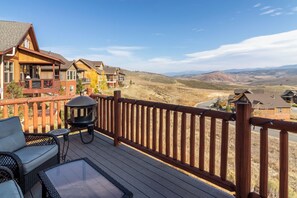 A wooden deck with outdoor furniture, a grill, and a view of a hilly landscape. - Beautiful 4-bedroom house in Granby perfect for your getaway (Granby)