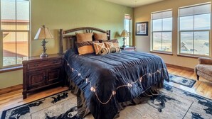 A bedroom with a large bed, a wooden headboard, a ceiling fan, and a view of the landscape through the windows. - Beautiful 4-bedroom house in Granby perfect for your getaway (Granby)
